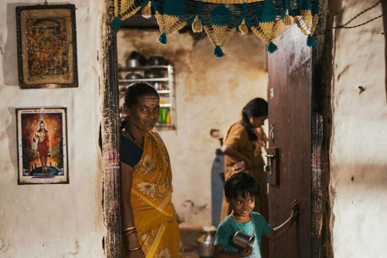 PMAY 2025 सूची की लाभार्थी संभावित महिला अपने पुराने झोपड़ीनुमा घर के सामने